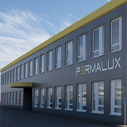 Firmengebäude PERMALUX Graues Firmengebäude von PERMALUX mit Eingangsbereich und Logo PERMALUX